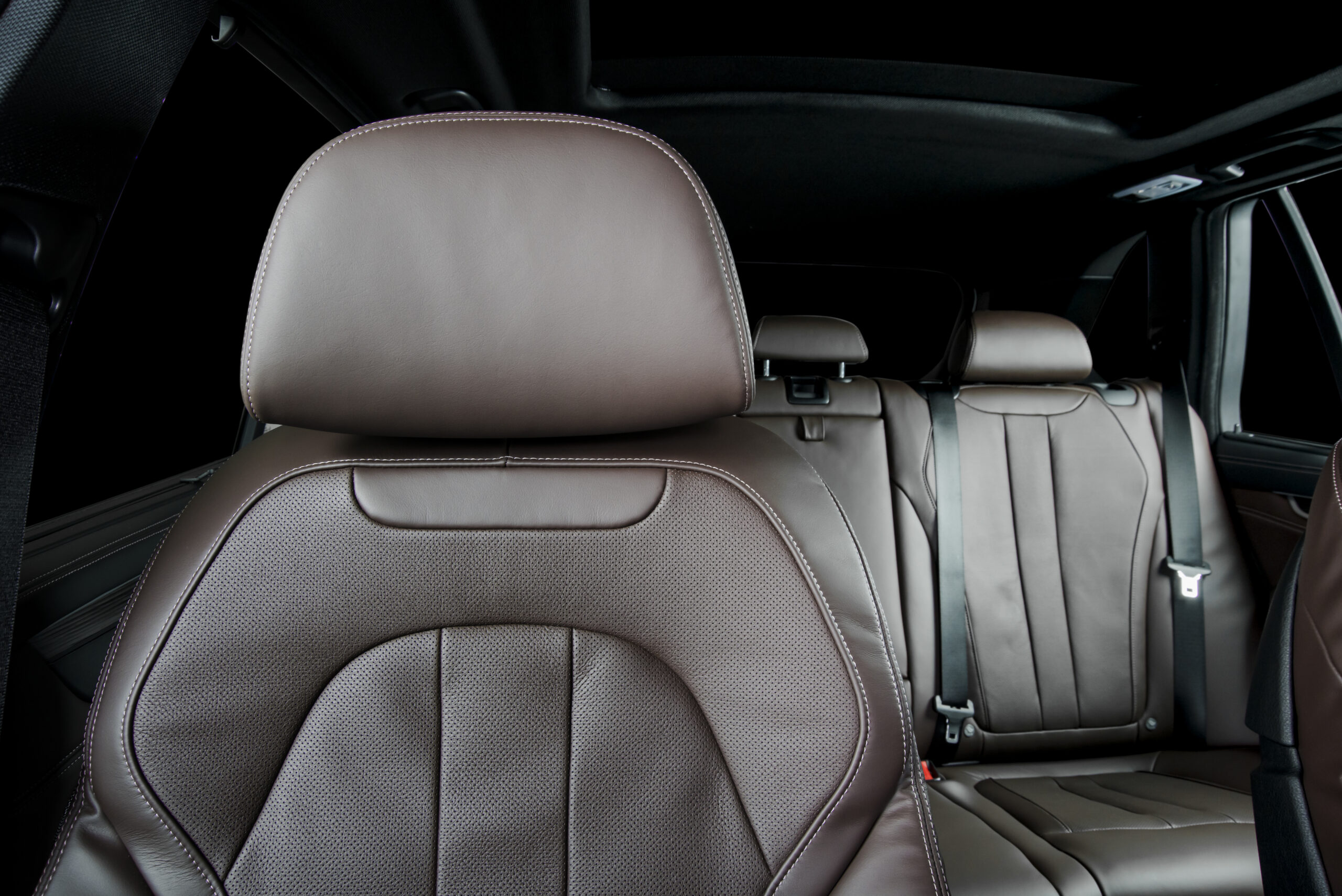 Modern luxury car  brown perforated leather interior. Part of  leather car headrest seat details. Back seats in background